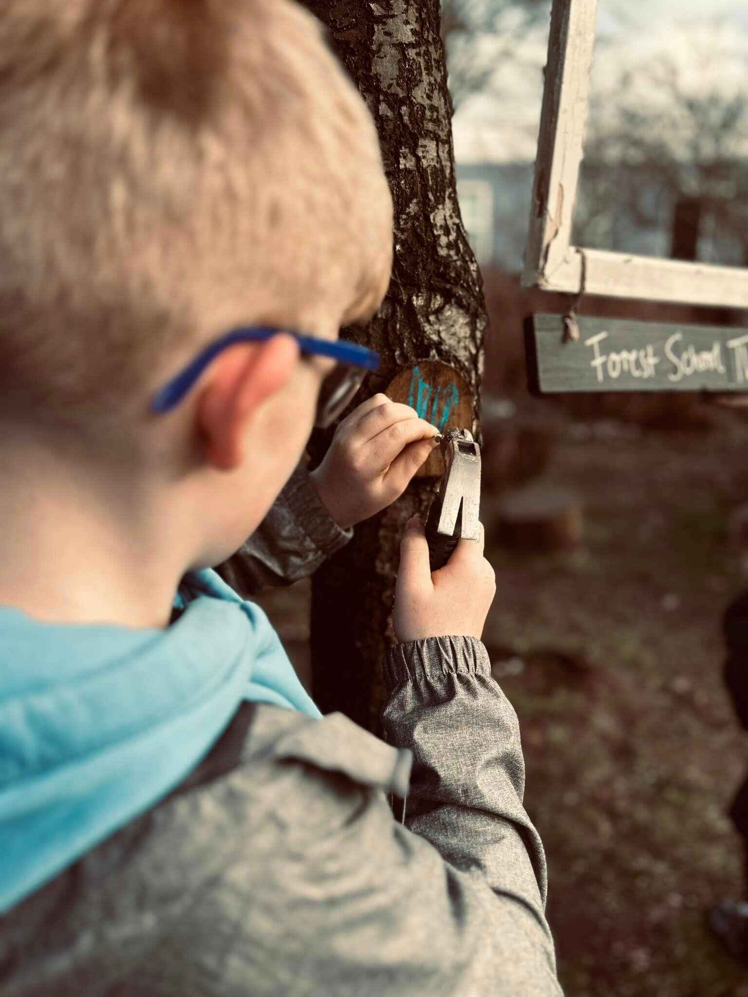 Child hammering nail into tree